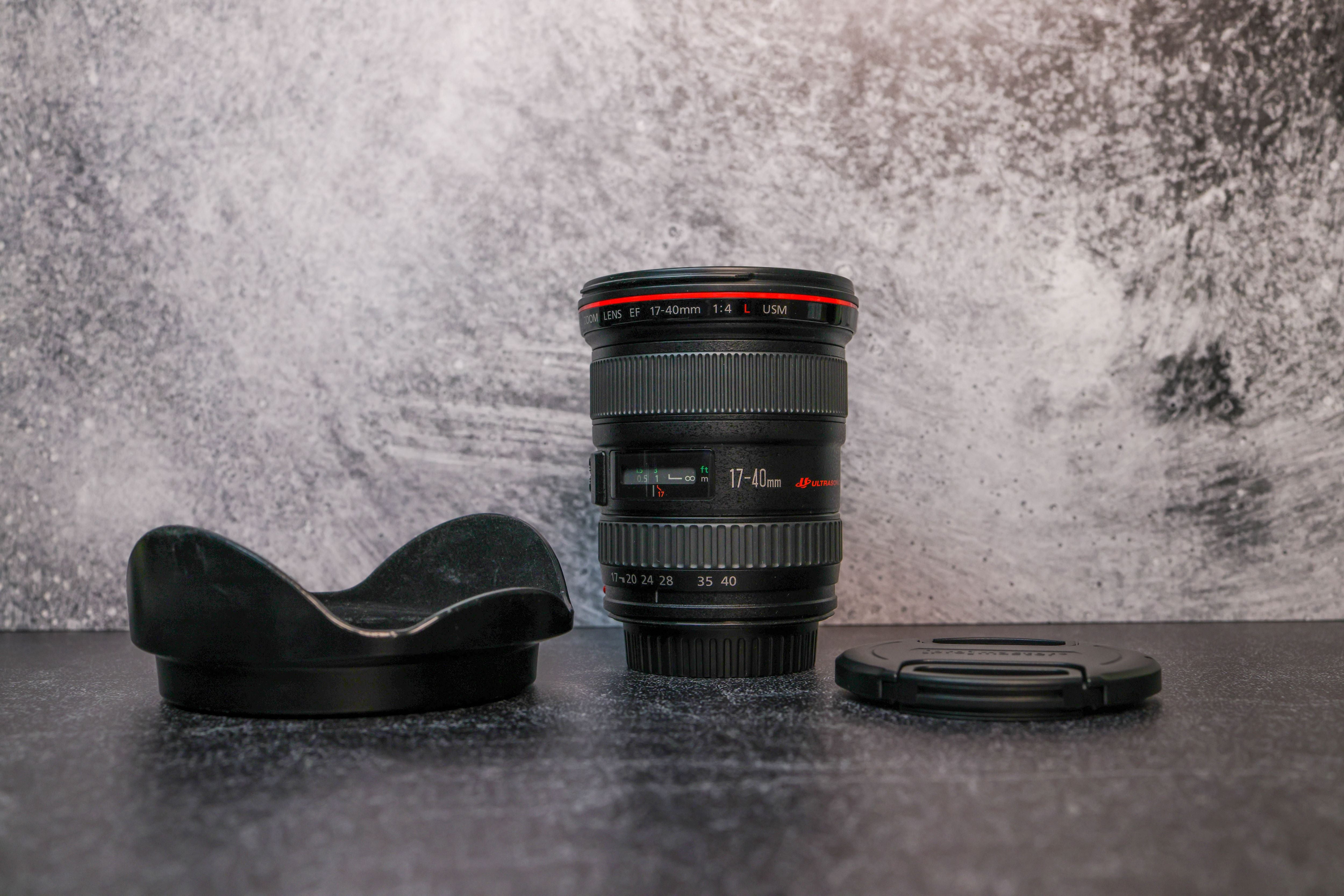 Canon 17-40 f/4.0 Camera Lens sitting vertically on the rear lens cap in the center, with the lens hood and cap sitting on either side