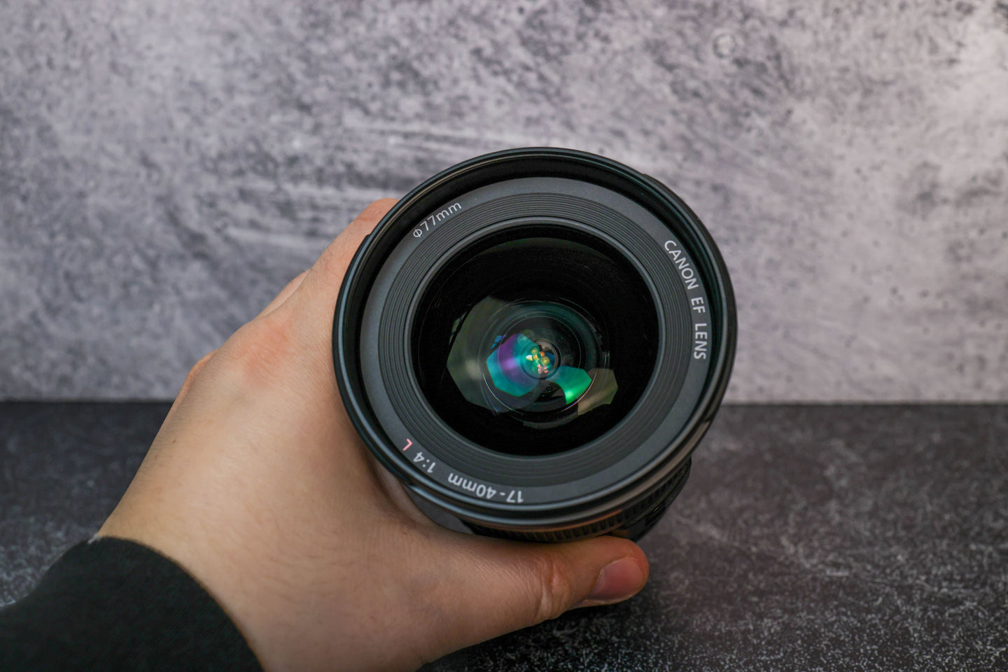 A hand holding the Canon 17-40 f/4.0 camera lens to show the front glass element