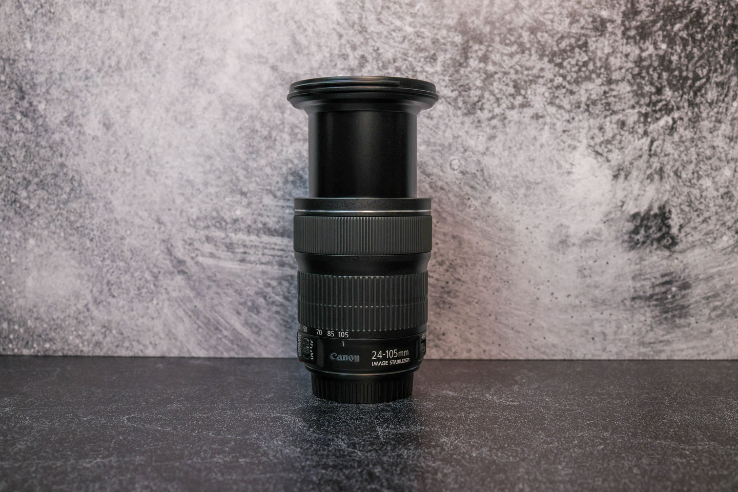 A Canon 24-105mm lens fully extended to show the zoom range sitting vertically on the rear lens cap